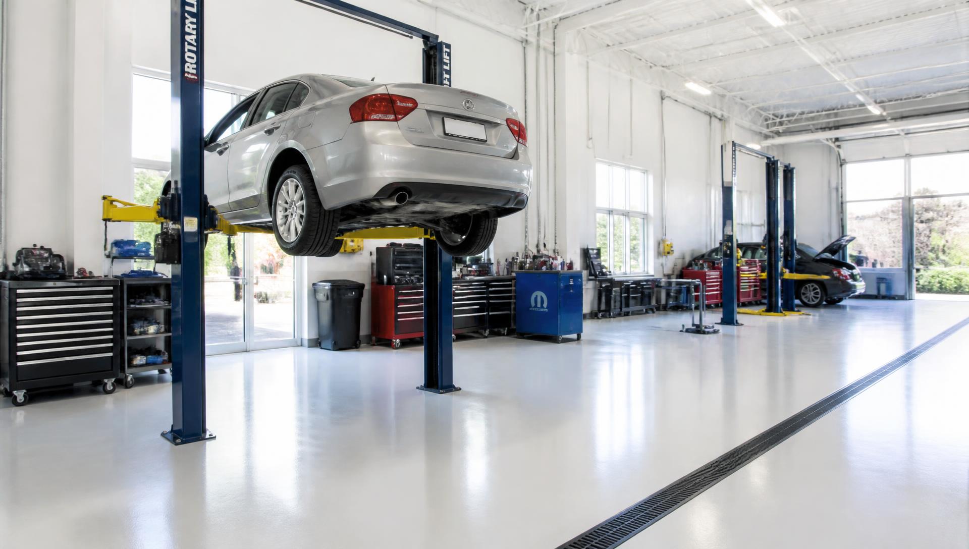 A silver sedan on a lift inside a bright, professional auto repair shop